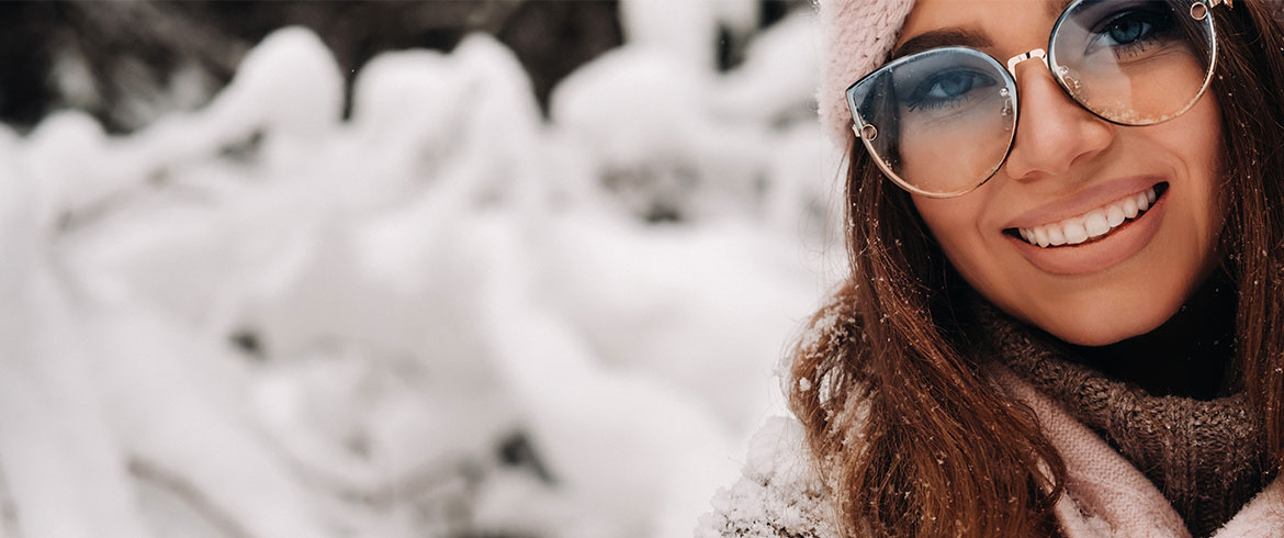 Eine Frau in schneebedeckter Landschaft mit Sonnenbrille zeigt die Bedeutung von Sonnenschutz auch im Winter, um die Haut vor UV-Strahlung zu schützen.